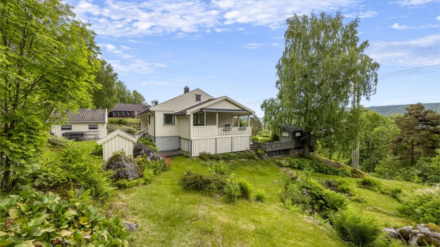 Eiendommen ligger i et svakt skrånende terreng, omkranset av natur og hage.