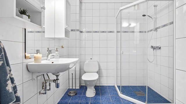 Bad i underetasjen med flislagt gulv, gulvvarme, dusjhjørne og toalett.