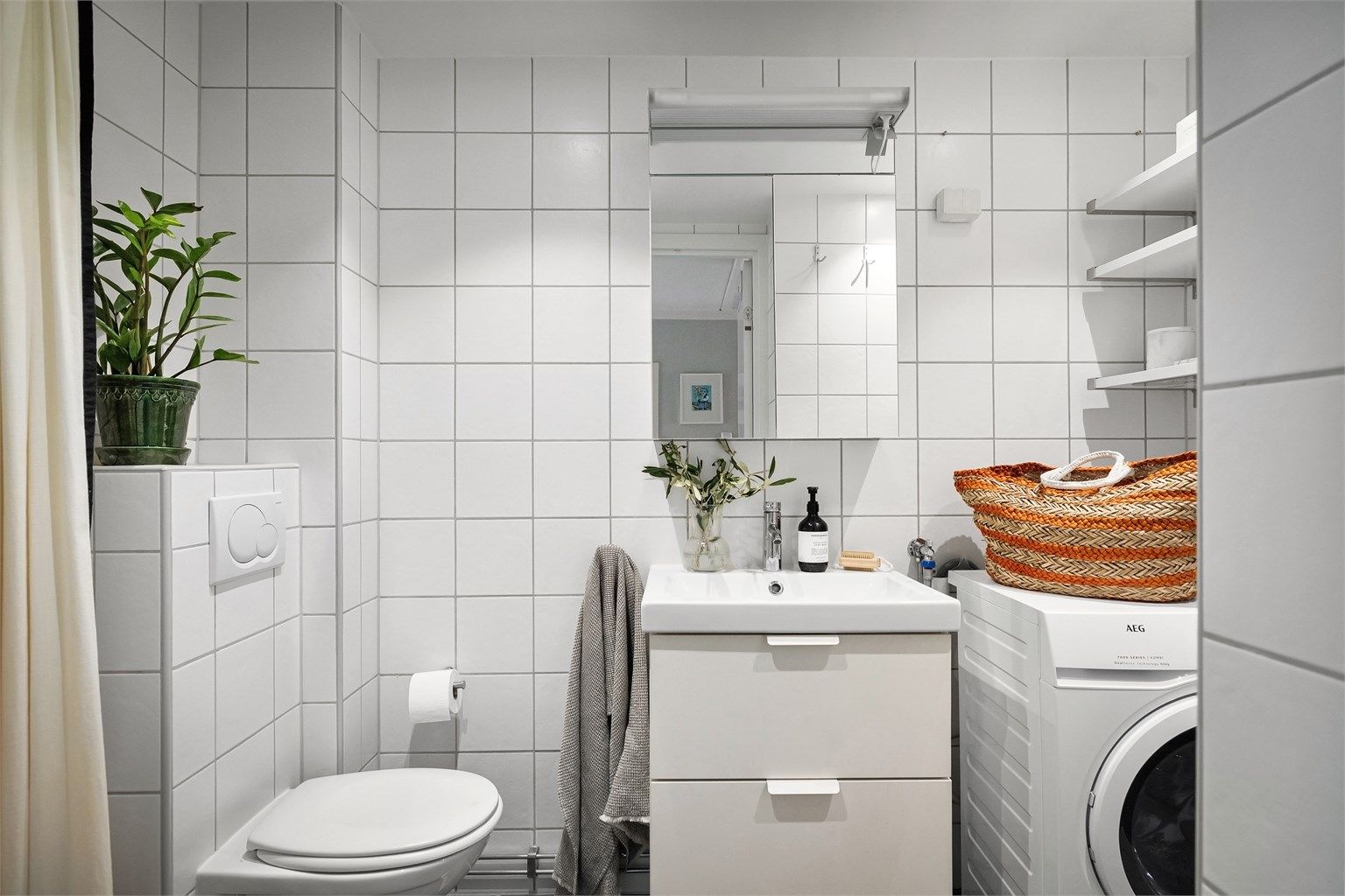  Badet er utstyrt med vegghengt toalett og heldekkende servant med skuffeinnredning under og speilskap med overlys på vegg