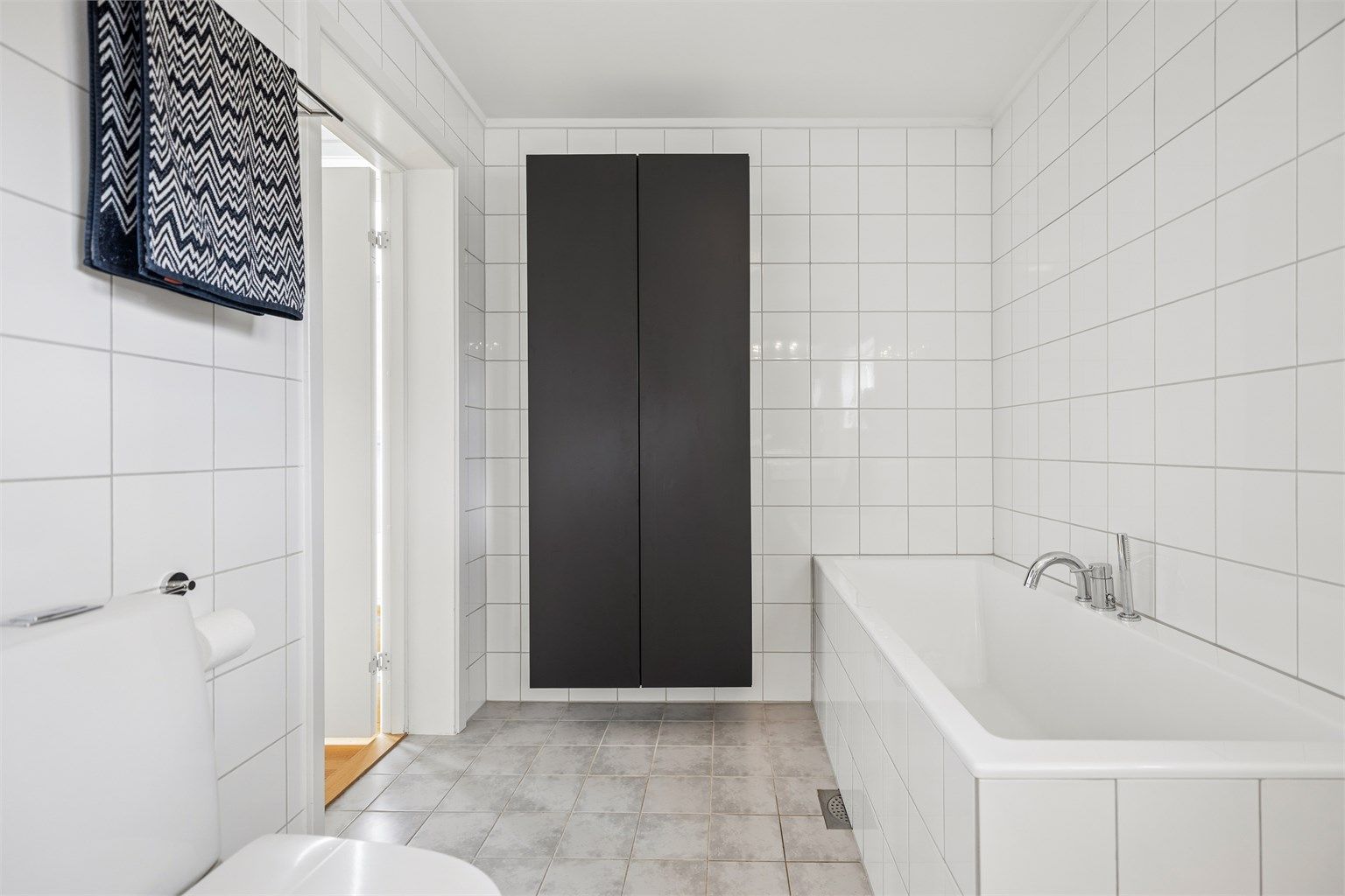 Badet er utstyrt med flislagt badekar og praktisk vegghengt baderomsinnredning som gir gode oppbevaringsmuligheter.