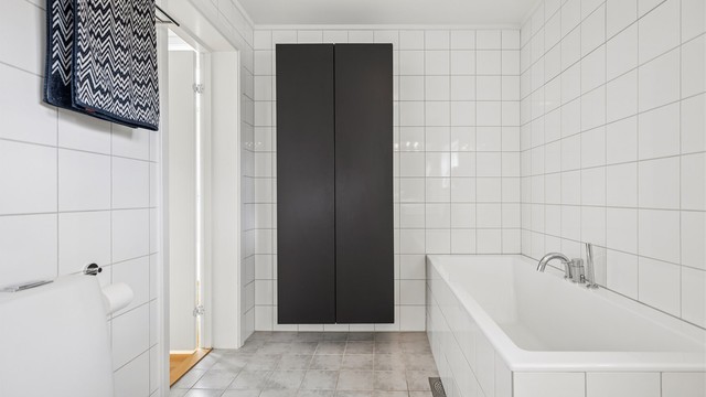Badet er utstyrt med flislagt badekar og praktisk vegghengt baderomsinnredning som gir gode oppbevaringsmuligheter.