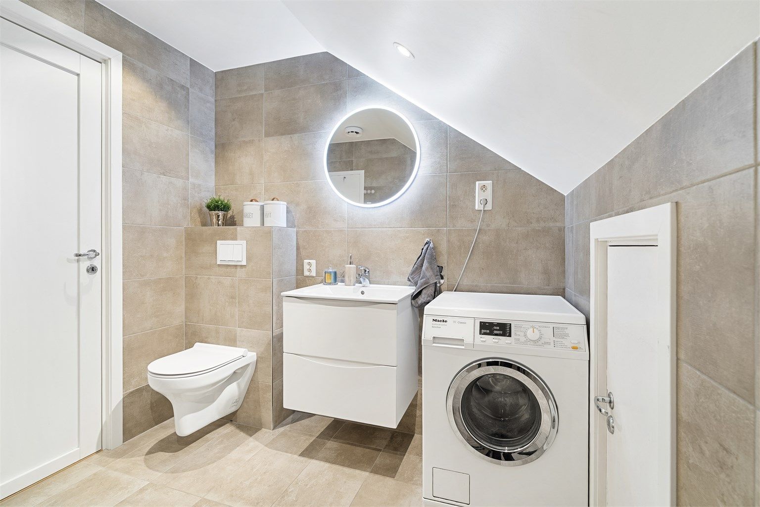 Badet er innredet med veggehengt servantskap med skuffer, speil med lys og stikkontakt på vegg over servant, nedsenket dusjssone og vegghengt toalett