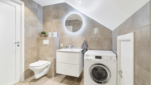 Badet er innredet med veggehengt servantskap med skuffer, speil med lys og stikkontakt på vegg over servant, nedsenket dusjssone og vegghengt toalett