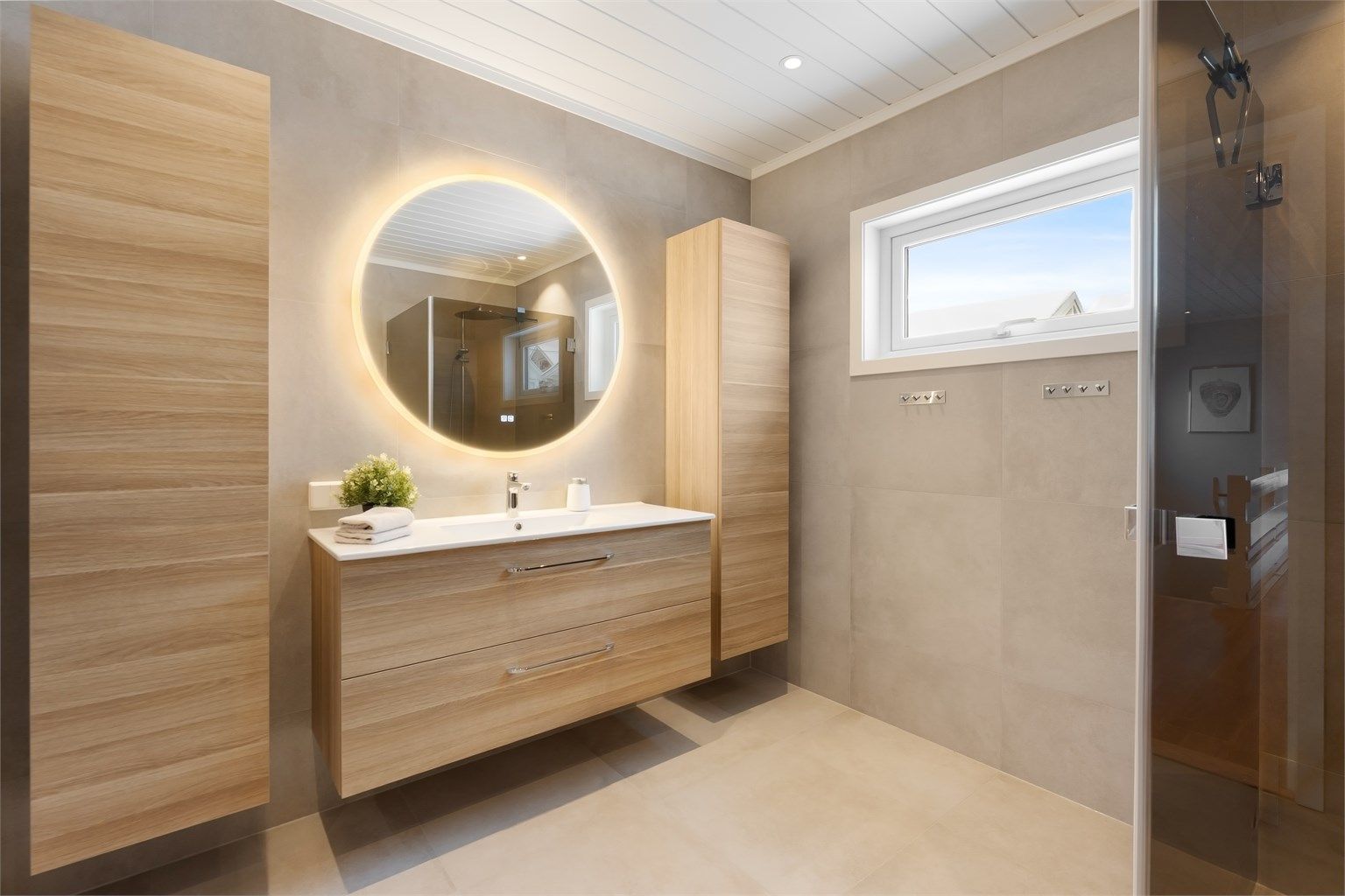 Innredningen inkluderer en bred, vegghengt servant med skuffer og et speil med integrert belysning.