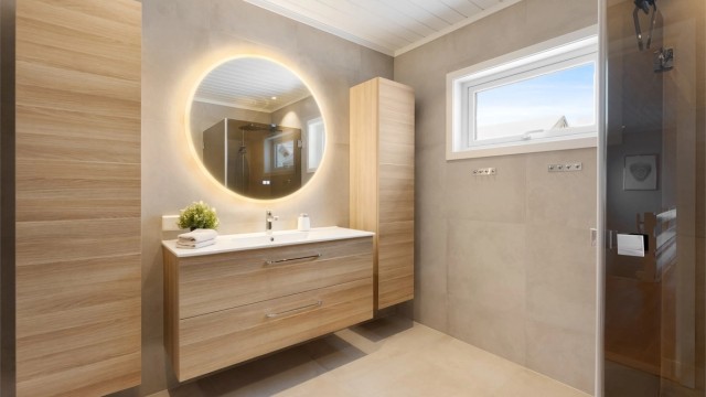 Innredningen inkluderer en bred, vegghengt servant med skuffer og et speil med integrert belysning.