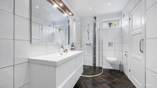 Badet i underetasjen har fliser på gulv og vegger, og er utstyrt med dusjvegger, toalett og en servant nedfelt i innredningen.