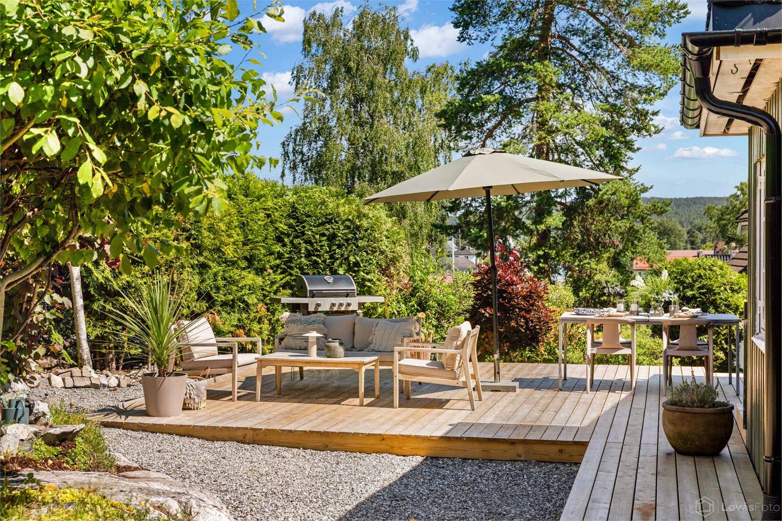 Terrassen ligger skjermet til og omkranses av en frodig, opparbeidet hage med trær, naturstein og variert beplantning som skaper en lun og privat atmosfære.