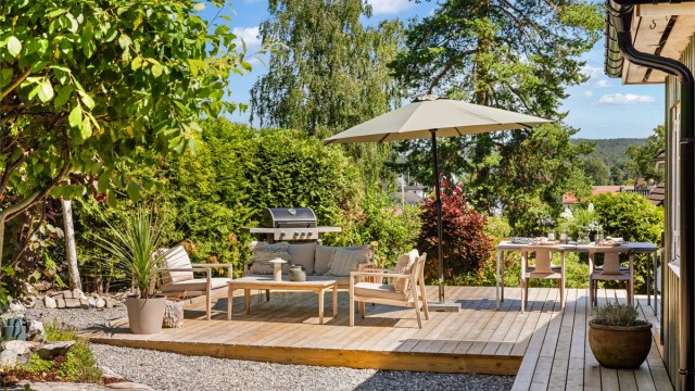 Terrassen ligger skjermet til og omkranses av en frodig, opparbeidet hage med trær, naturstein og variert beplantning som skaper en lun og privat atmosfære.
