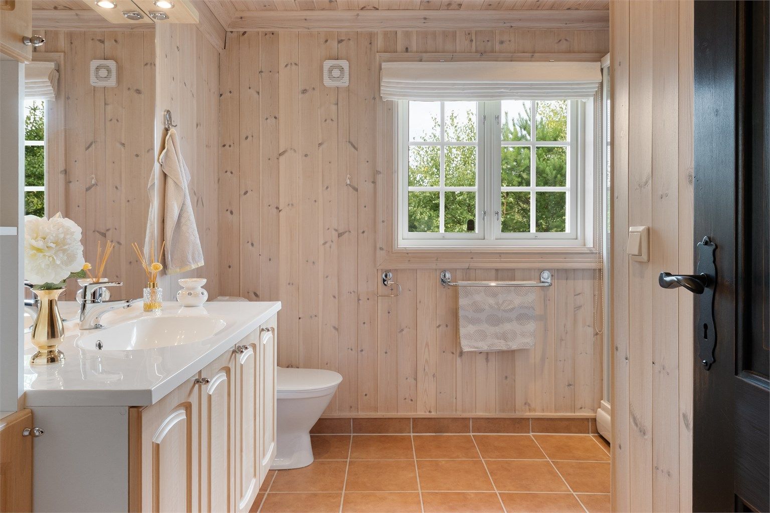 Badet har flislagt gulv med gulvvarme, beisede panelvegger, servantinnredning, dusjkabinett og toalett.