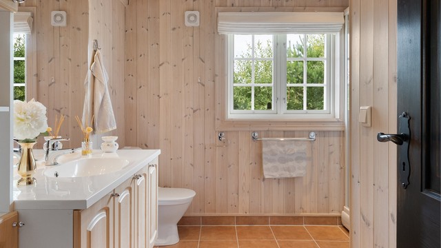 Badet har flislagt gulv med gulvvarme, beisede panelvegger, servantinnredning, dusjkabinett og toalett.