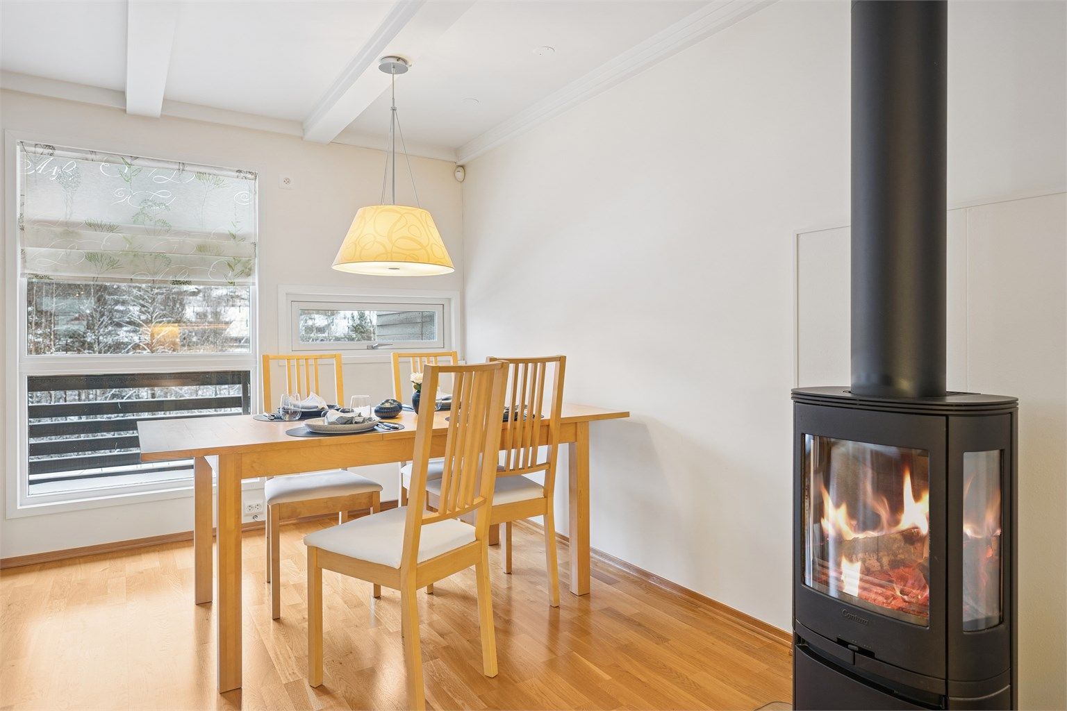 Stuen får godt med naturlig lys fra store vinduer, og den moderne peisovnen bidrar til en koselig og varm atmosfære.