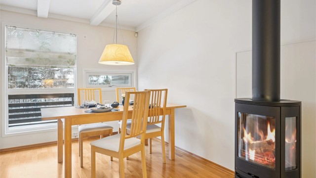 Stuen får godt med naturlig lys fra store vinduer, og den moderne peisovnen bidrar til en koselig og varm atmosfære.