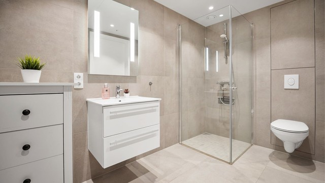 Stilrent bad 1 med store flisoverflater, ved entré. Badet har dusjhjørne med innfellbare dusjdører av glass.