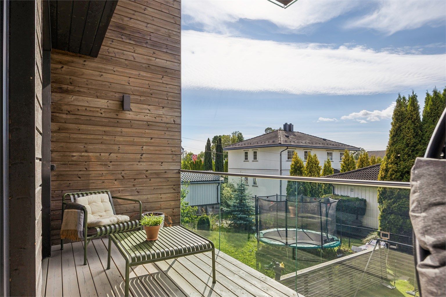 Balkong med utgang fra stuen, belagt med terrassebord og rekkverk i glass.