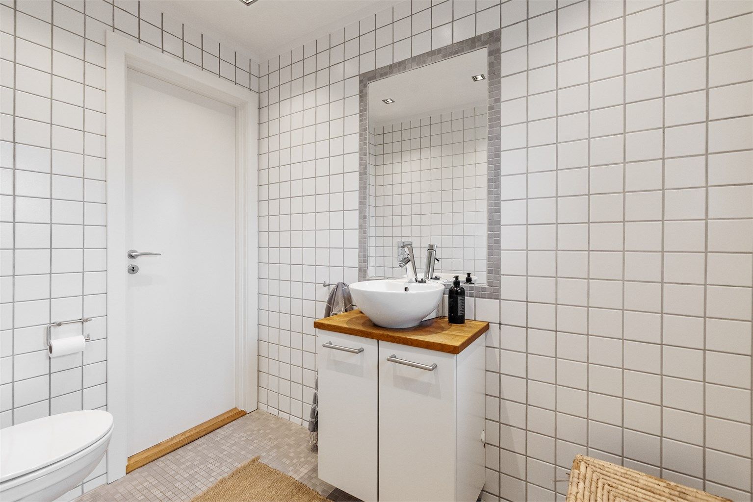 Badet er utstyrt med vegghengt toalett og servantinnredning med skapdører og ovenpåliggende servant