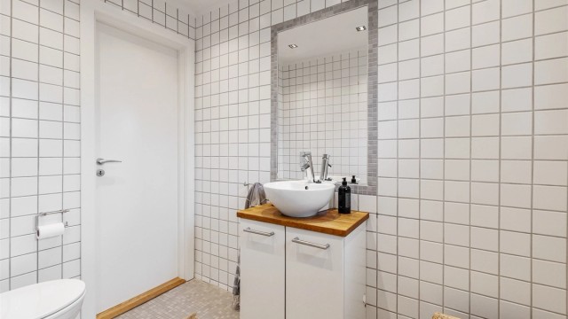 Badet er utstyrt med vegghengt toalett og servantinnredning med skapdører og ovenpåliggende servant
