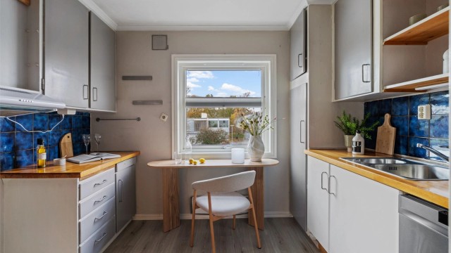 Kjøkken med innredning fra byggeår, benkeplate i tre og vindu mot nabolaget.