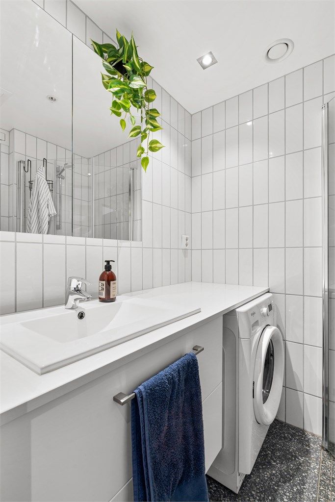 Baderommet er innredet med vegghengt servant, speilskap, dusjhjørne, vegghengt toalett og opplegg for vaskemaskin.