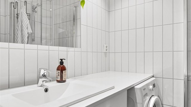 Baderommet er innredet med vegghengt servant, speilskap, dusjhjørne, vegghengt toalett og opplegg for vaskemaskin.