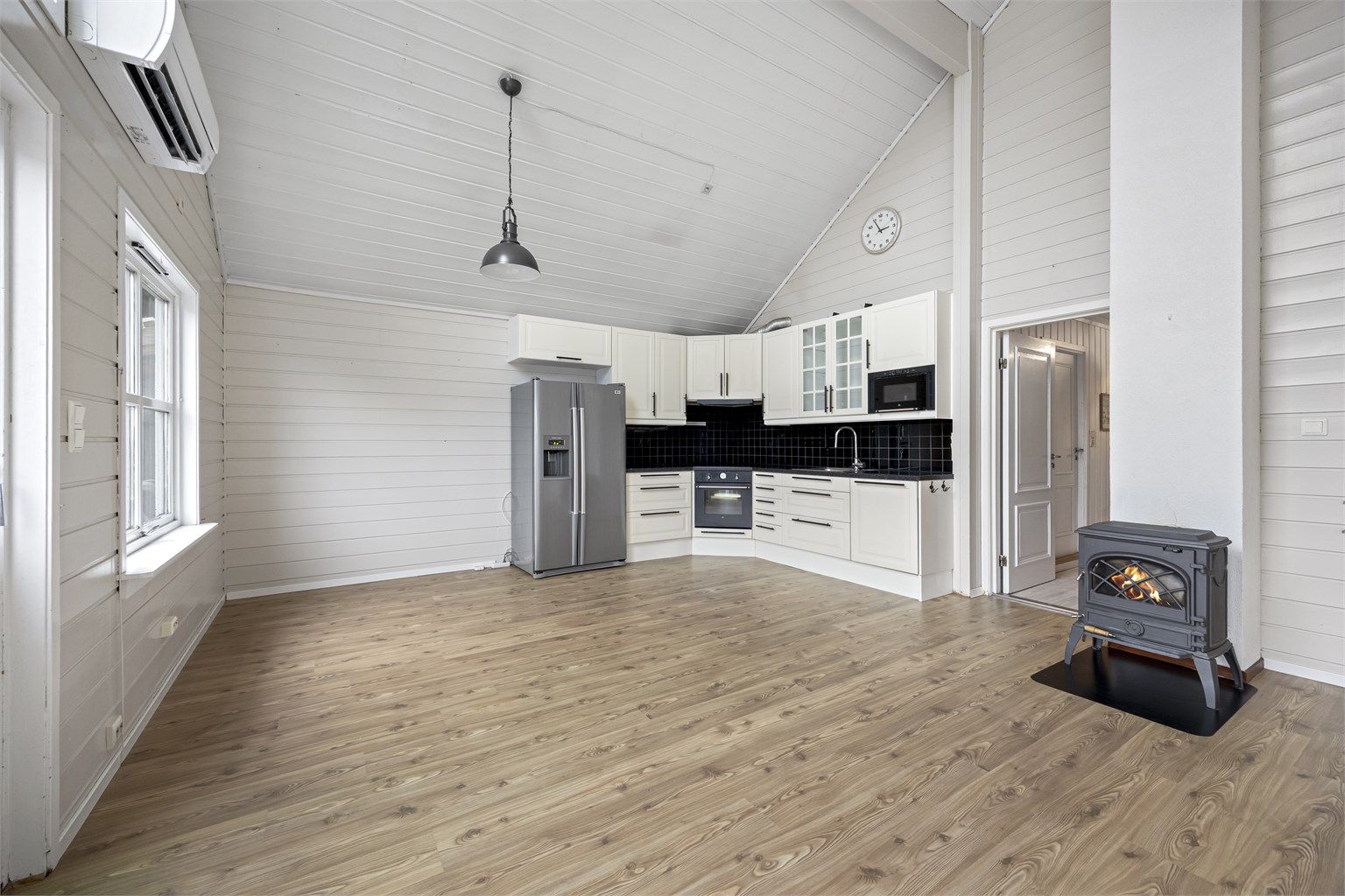 Den åpne løsningen mellom stue og kjøkken skaper en sosial atmosfære, med en peisovn som et sentralt samlingspunkt.