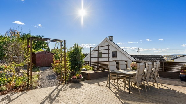 Terrasseplattingen har overgang til hageområde med gruset sti bort til en frittstående utebod.