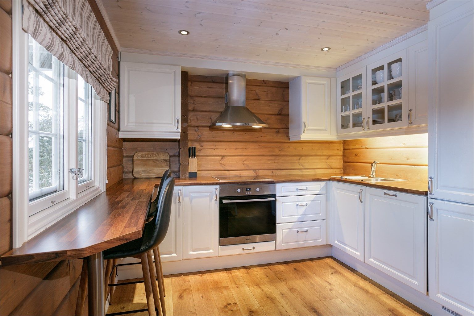 Romslig kjøkken med hvit profilert kjøkkeninnredning med benkeplate av laminat. Det er kjøl/fryseskap, oppvaskmaskin, platetopp og stekeovn.