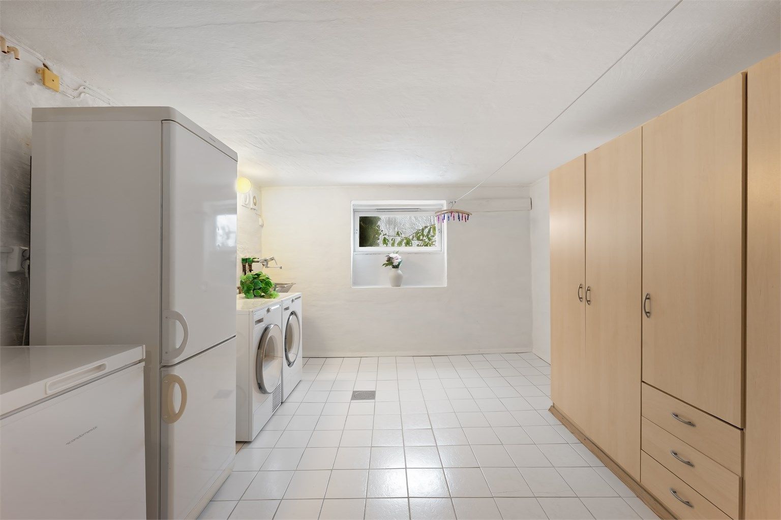 Stort, separat vaskerom med flislagt gulv, utslagsvask og opplegg for vaskemaskin.