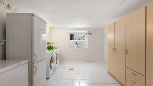 Stort, separat vaskerom med flislagt gulv, utslagsvask og opplegg for vaskemaskin.