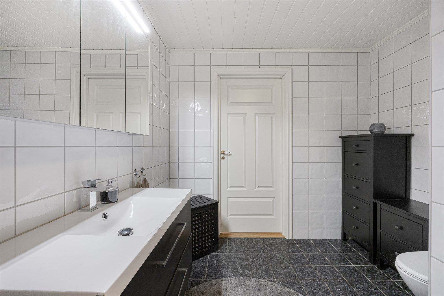 Heldekkende servant over servantskap med glatte, folierte fronter. Varmtvannsberederen på 194 liter fra 2008 er plassert på badet.