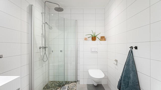 Pent flislagt baderom i tilknytning til hovedsoverommet, med dusjhjørne med glassdører og gulv belagt med elvestein. Videre er det vegghengt toalett og servant med innredning. Rommet varmes opp med vannbåren varme.