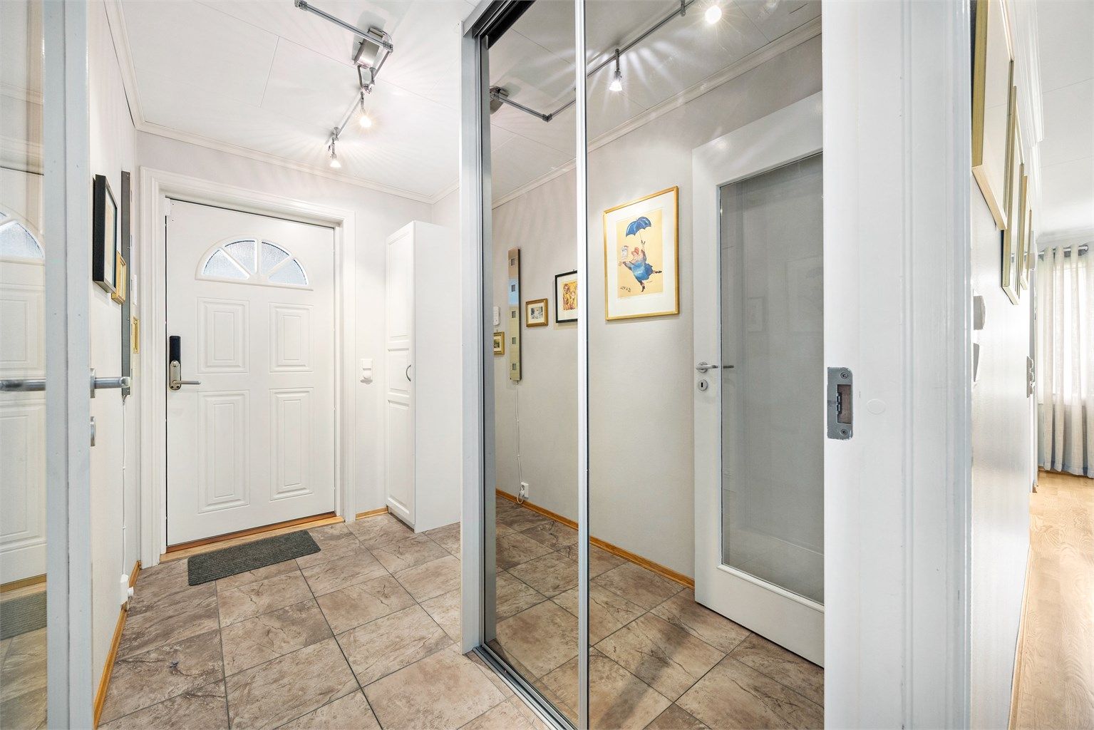 Entré med flislagt gulv og skyvedørsgarderobe med speilfronter.