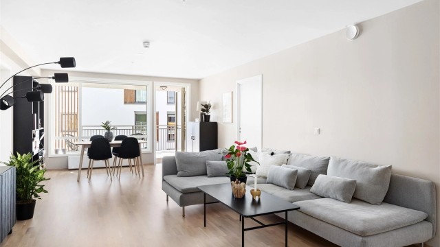 Åpen stue- og kjøkkenløsning. Leiligheten har hovedsakelig tre-stavs eikeparkett på gulv, vegger og himlinger med malte, slette flater. Slette innerdører. Foto: Christian Thorsbye - Diakrit