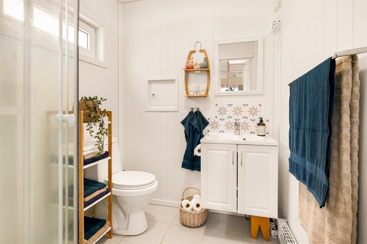 Bad med flislagt gulv, wc, servant i seksjon og dusjkabinett.