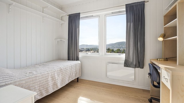 Lyst og trivelig soverom med praktiske, veggmonterte hyller.