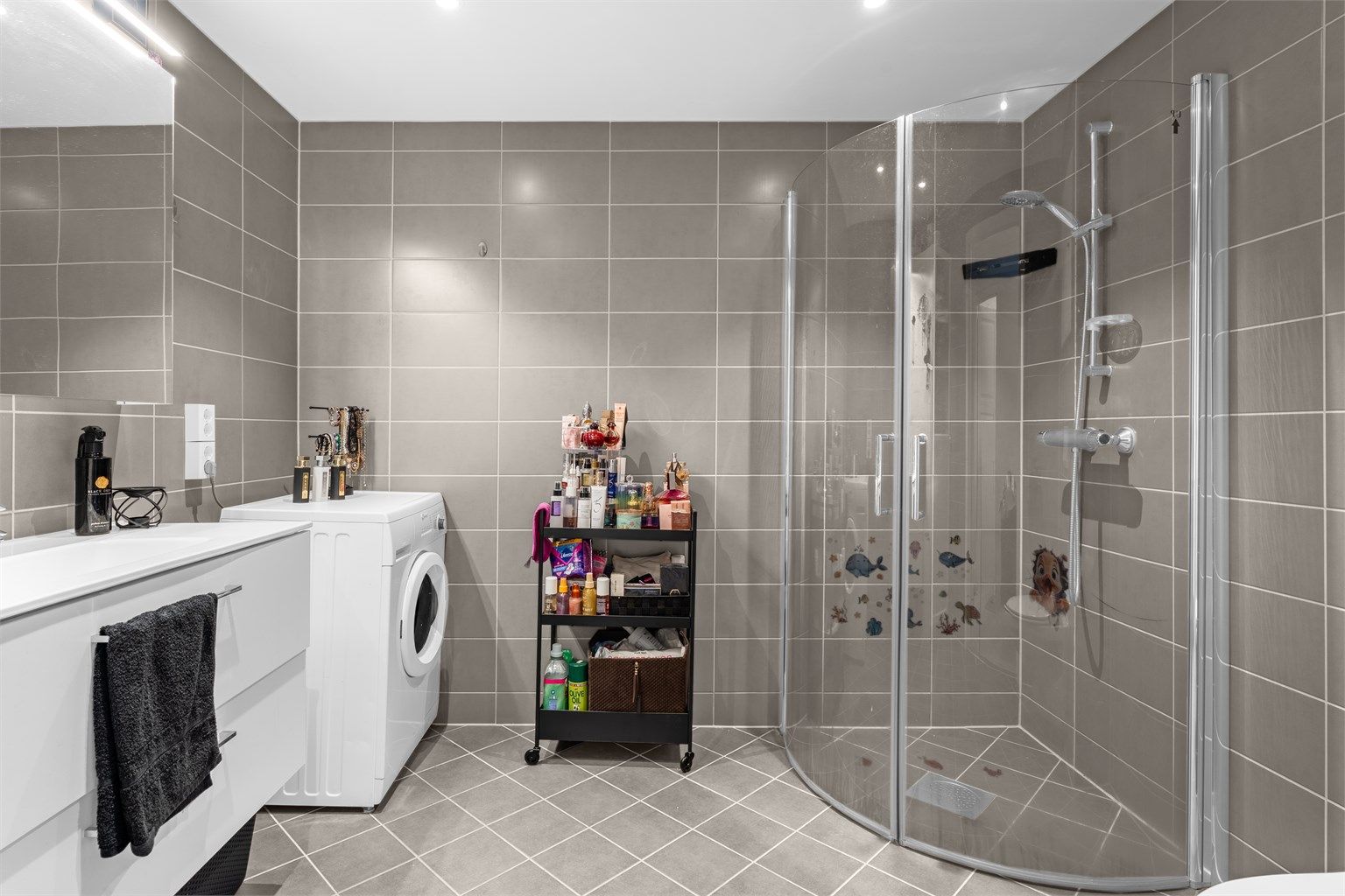 Badet har buede dusjdører i glass. Det er opplegg for vaskemaskin og ev. tørketrommel