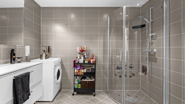 Badet har buede dusjdører i glass. Det er opplegg for vaskemaskin og ev. tørketrommel
