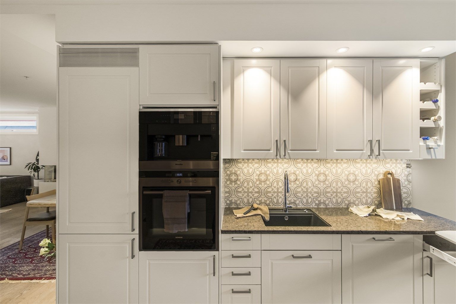 Delikat flisevalg under overskapene og praktisk med downlights over kjøkkenbenk og detaljer med lys i sokkelen