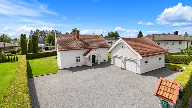 Stor, gruset gårdsplass med rikelig av biloppstillingsplasser foran huset og garasjen.