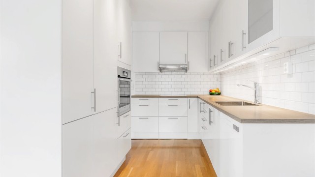 Åpen kjøkkenløsning. Innredning fra byggeår. Glatte fronter. Benkeplate med laminert overflate. Kjøkkenvask med armatur.