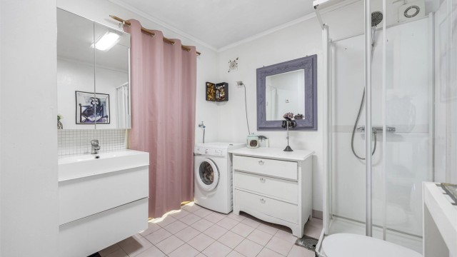 Badet er utstyrt med flislagt gulv med varmekabler, dusjkabinett, gulvstående toalett og opplegg for vaskemaskin.