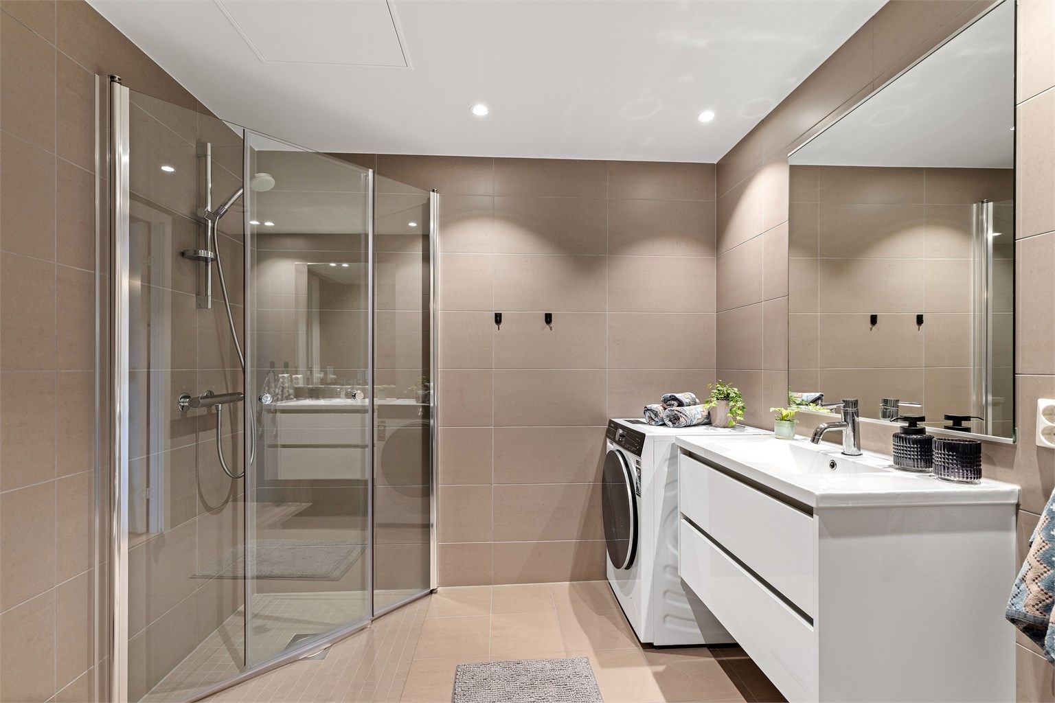 Vegghengt toalett og dusjhjørne med innfellbare glassdører, opplegg for vaskemaskin.