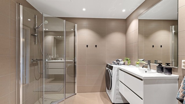 Vegghengt toalett og dusjhjørne med innfellbare glassdører, opplegg for vaskemaskin.