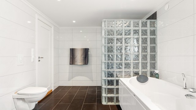 Badets generøse areal er utnyttet med et ekstra romslig dusjhjørne og et badekar med sitteplass for to. Gulv og vegger er flislagt, i gulvet er det varme.