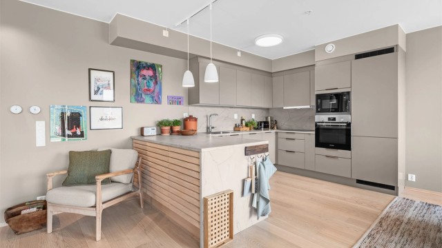 Kjøkkeninnredning med glatte fronter og laminert benkeplate. Godt med skap og benkeplass. Det er kjøkkenplate mellom benkeplate og overskap, overskapsbelysning og stikkontakter
