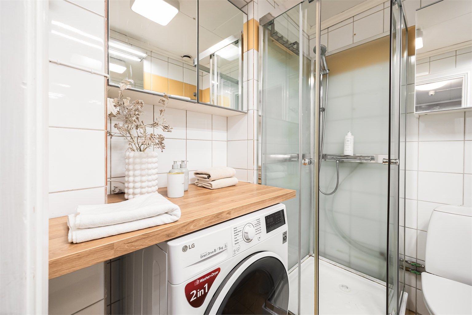 Videre er det speilskap på vegg over benkeplaten i tre som fungerer godt som en brettestasjon etter at klesvasken er tatt. Opplegg for vaskemaskin.