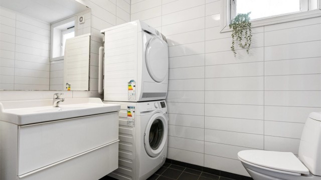 Badet har flislagt gulv med varme og baderomsplater på vegg samt opplegg for vaskemaskin og tørketrommel.