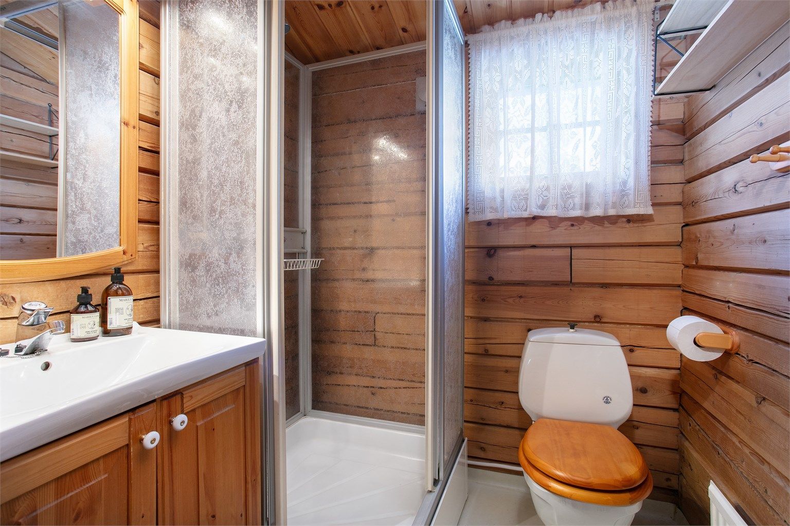 Badet er innredet med profilert furuinnredning, servant, toalett og dusjkabinett.