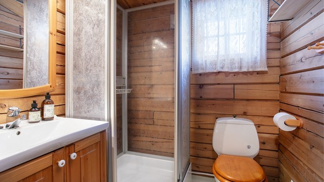 Badet er innredet med profilert furuinnredning, servant, toalett og dusjkabinett.