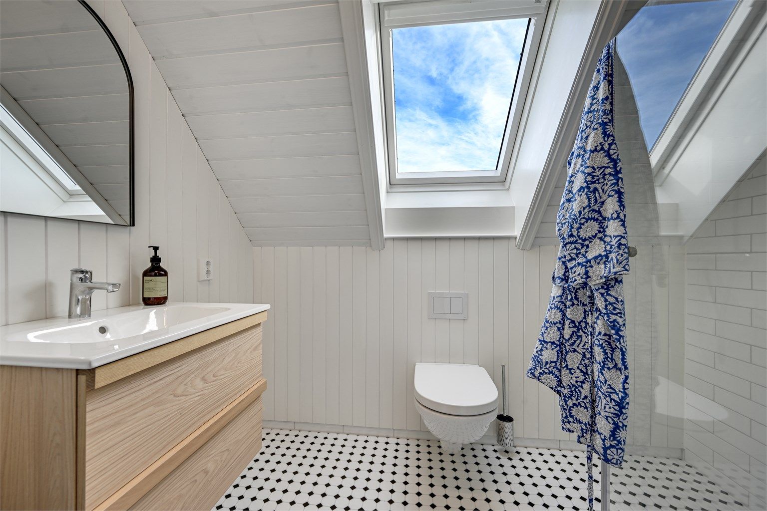 Badet har fliser på gulv og i dusjsonen, panel på øvrige vegger, elegante glassdører til dusjen, heldekkende servant og vegghengt toalett.