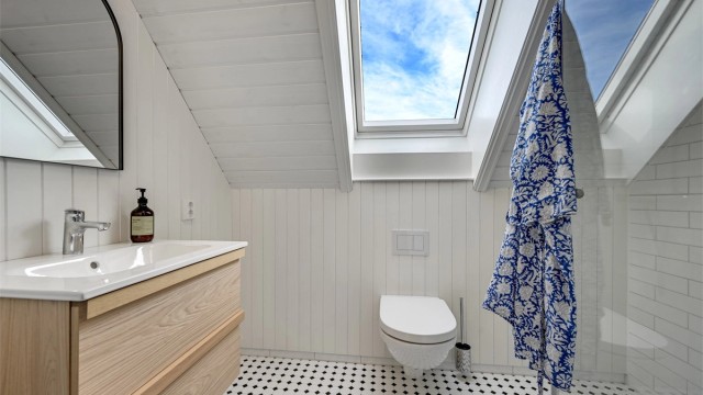 Badet har fliser på gulv og i dusjsonen, panel på øvrige vegger, elegante glassdører til dusjen, heldekkende servant og vegghengt toalett.